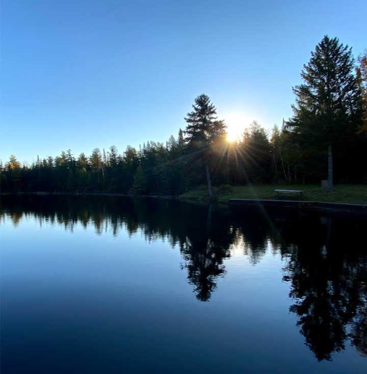 View of lake and shore. Sun peaking over trees